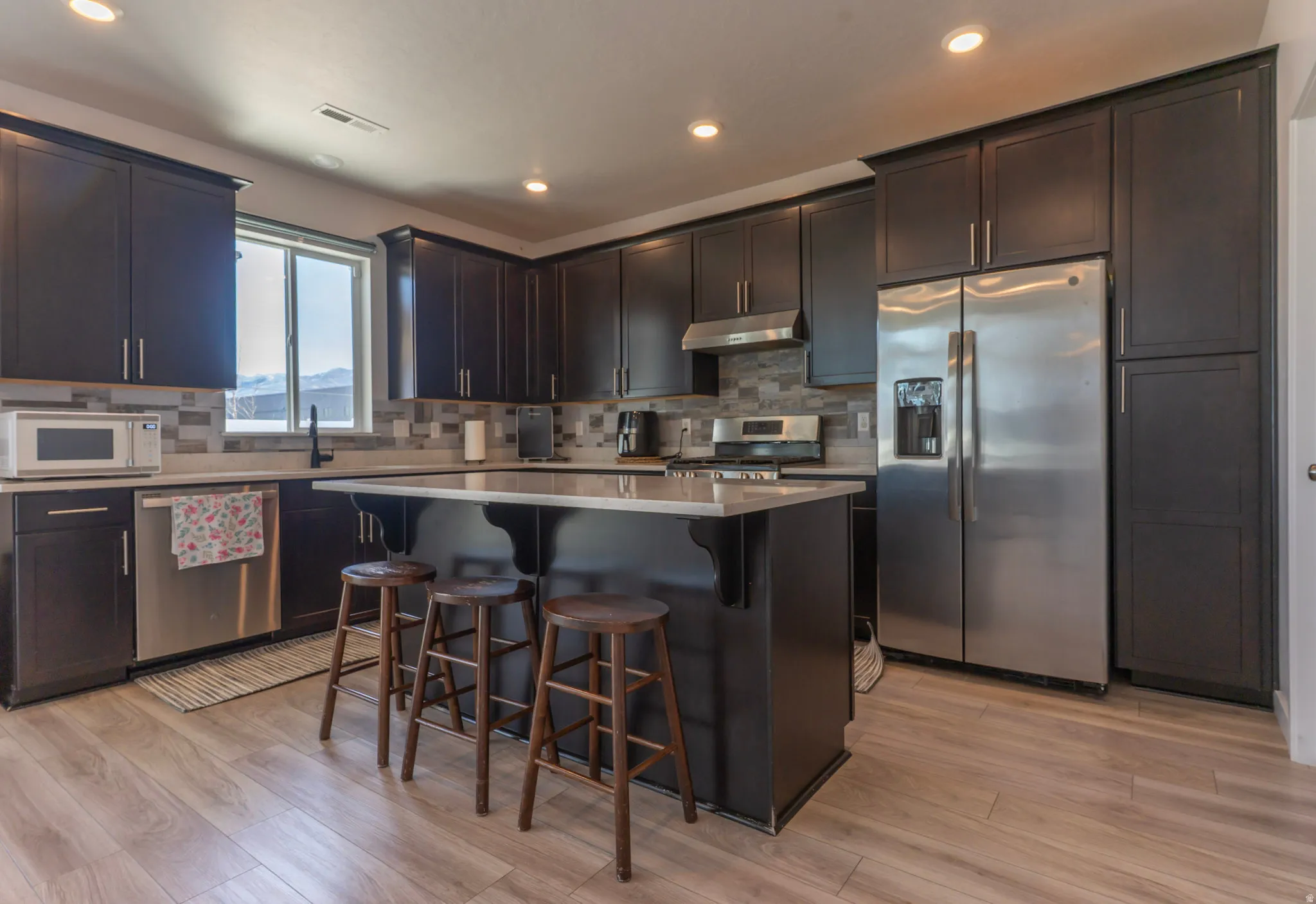 Kitchen featuring stainless steel appliances, a breakfast bar, a kitchen island, dark wood finish cabinetry, and light wood-style flooring