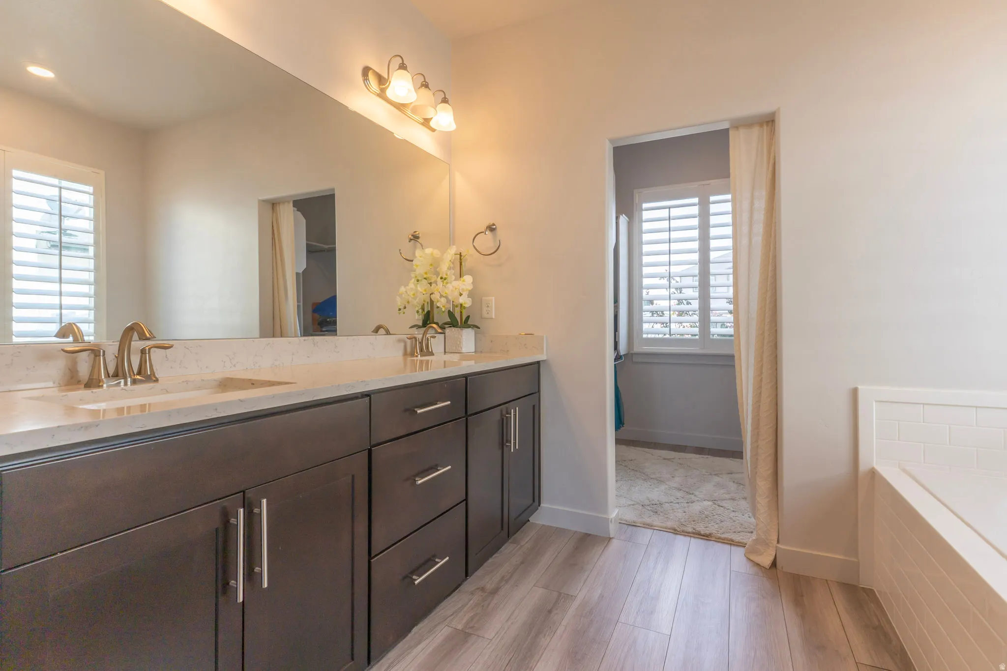 Bathroom featuring double vanity, light wood-type flooring, and a bath