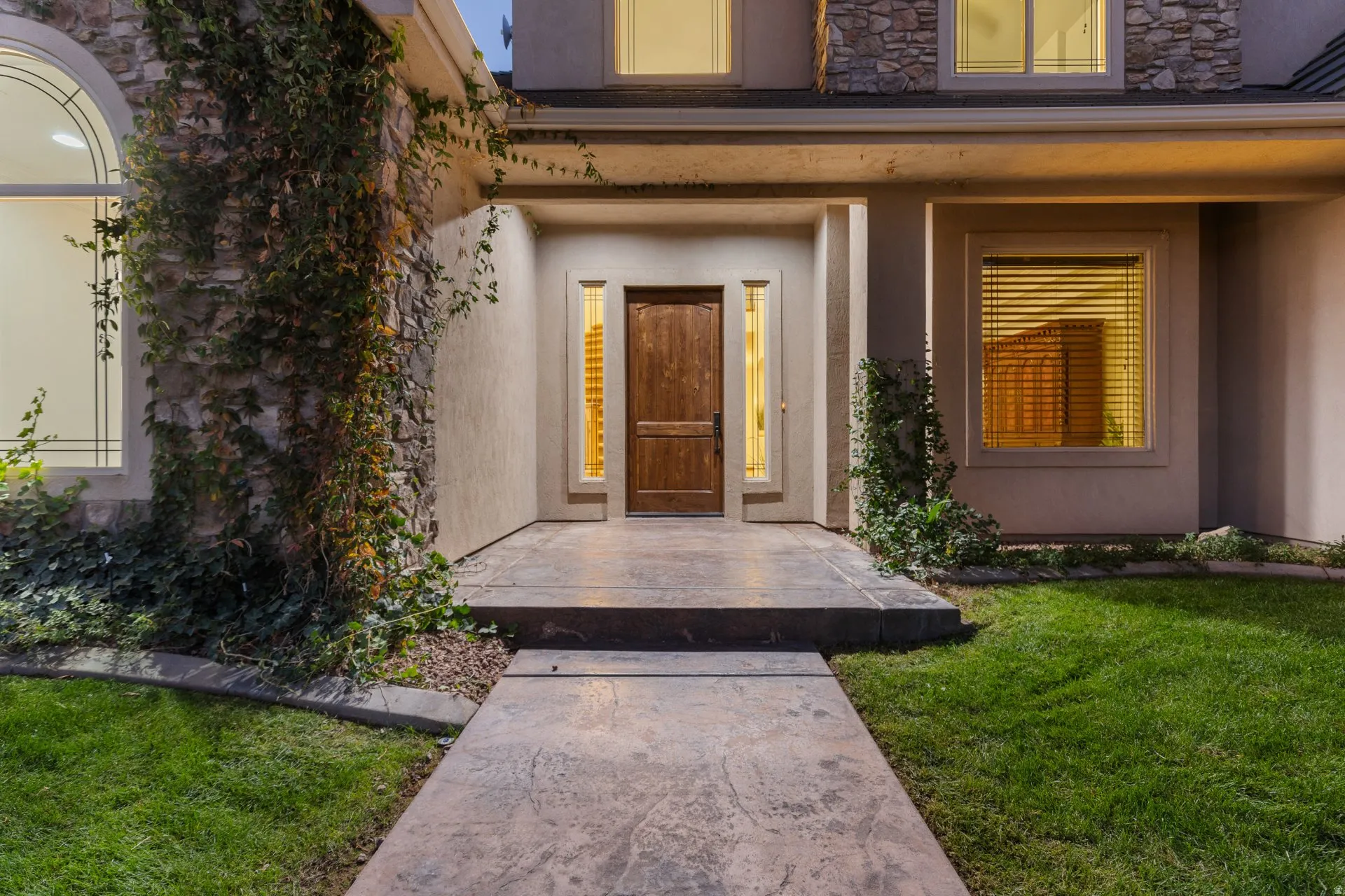 Doorway to property with stucco siding, stone siding, and a yard