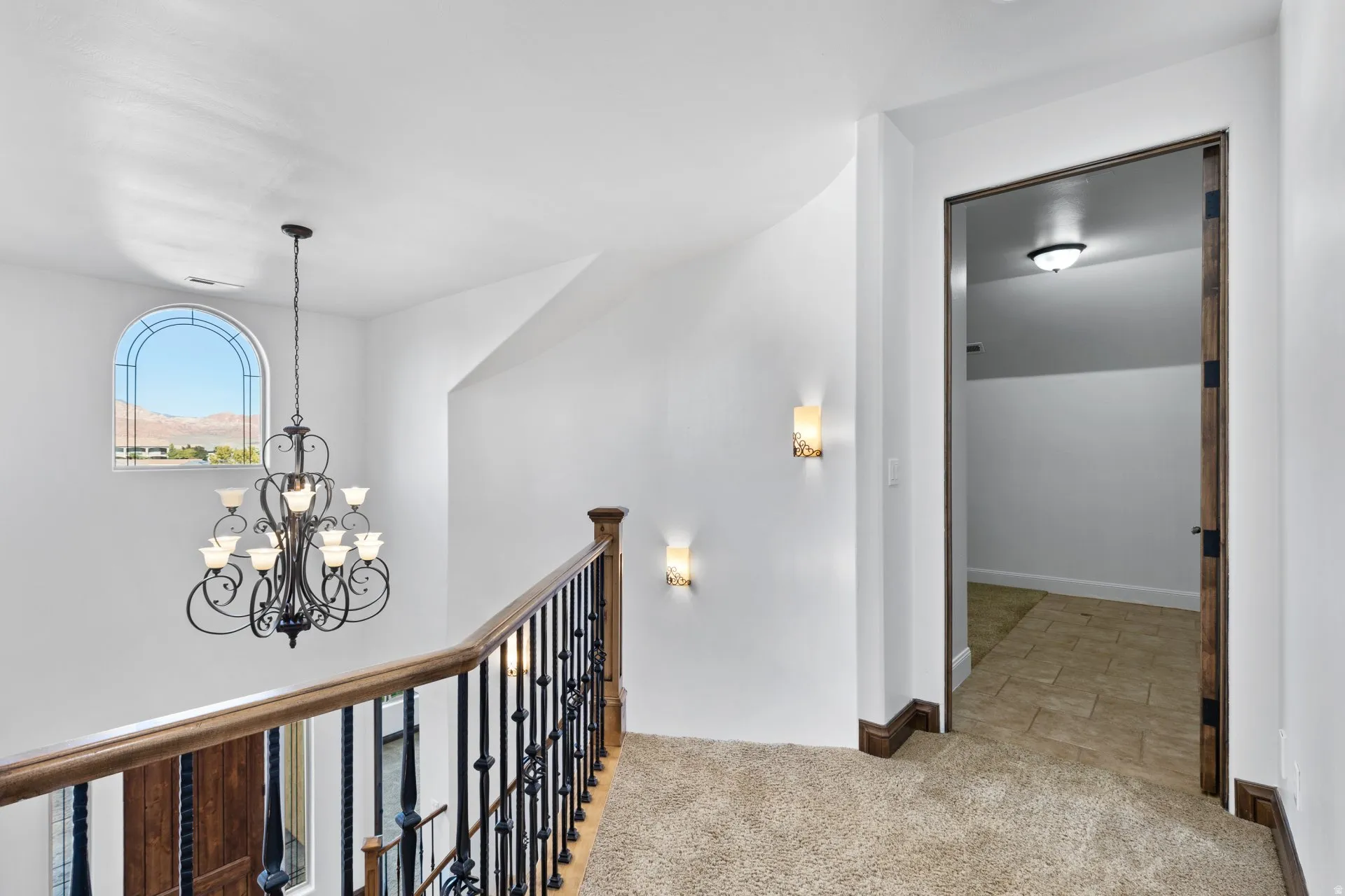 Hall with light colored carpet, a chandelier, and an upstairs landing