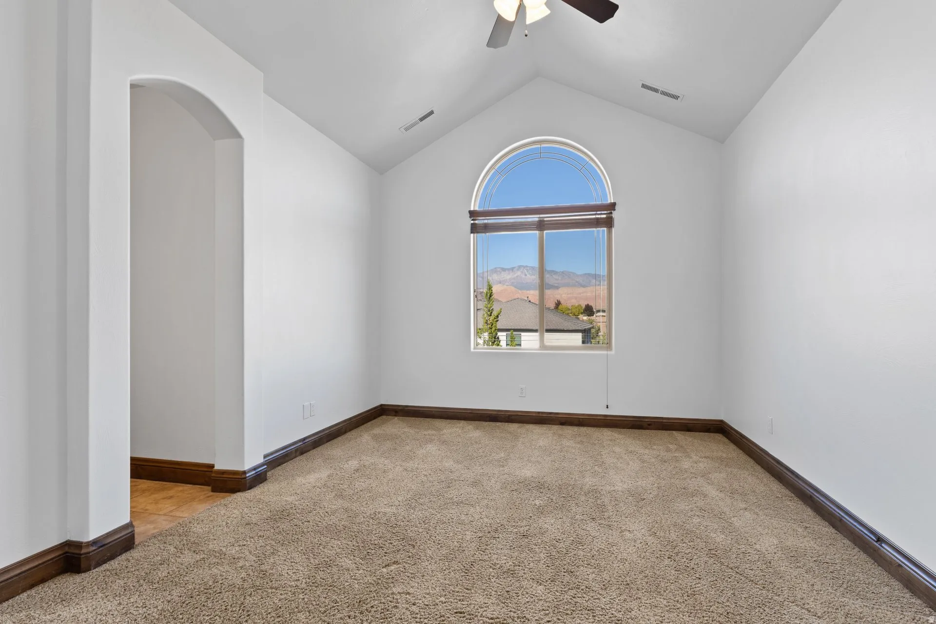 Unfurnished room with light colored carpet, ceiling fan, a mountain view, and arched walkways