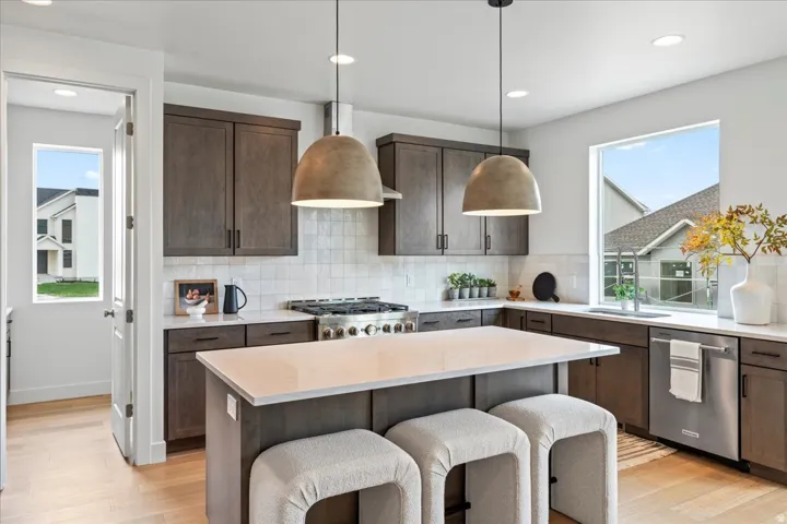 Kitchen featuring dark wood finish cabinetry, tasteful backsplash, decorative light fixtures, stainless steel appliances, and a center island