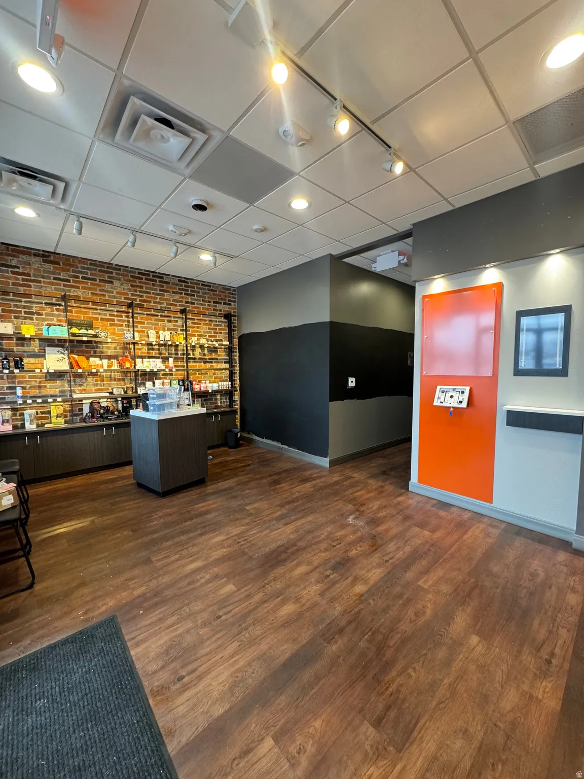 Reception featuring rail lighting, a drop ceiling, brick wall, and bar with sink
