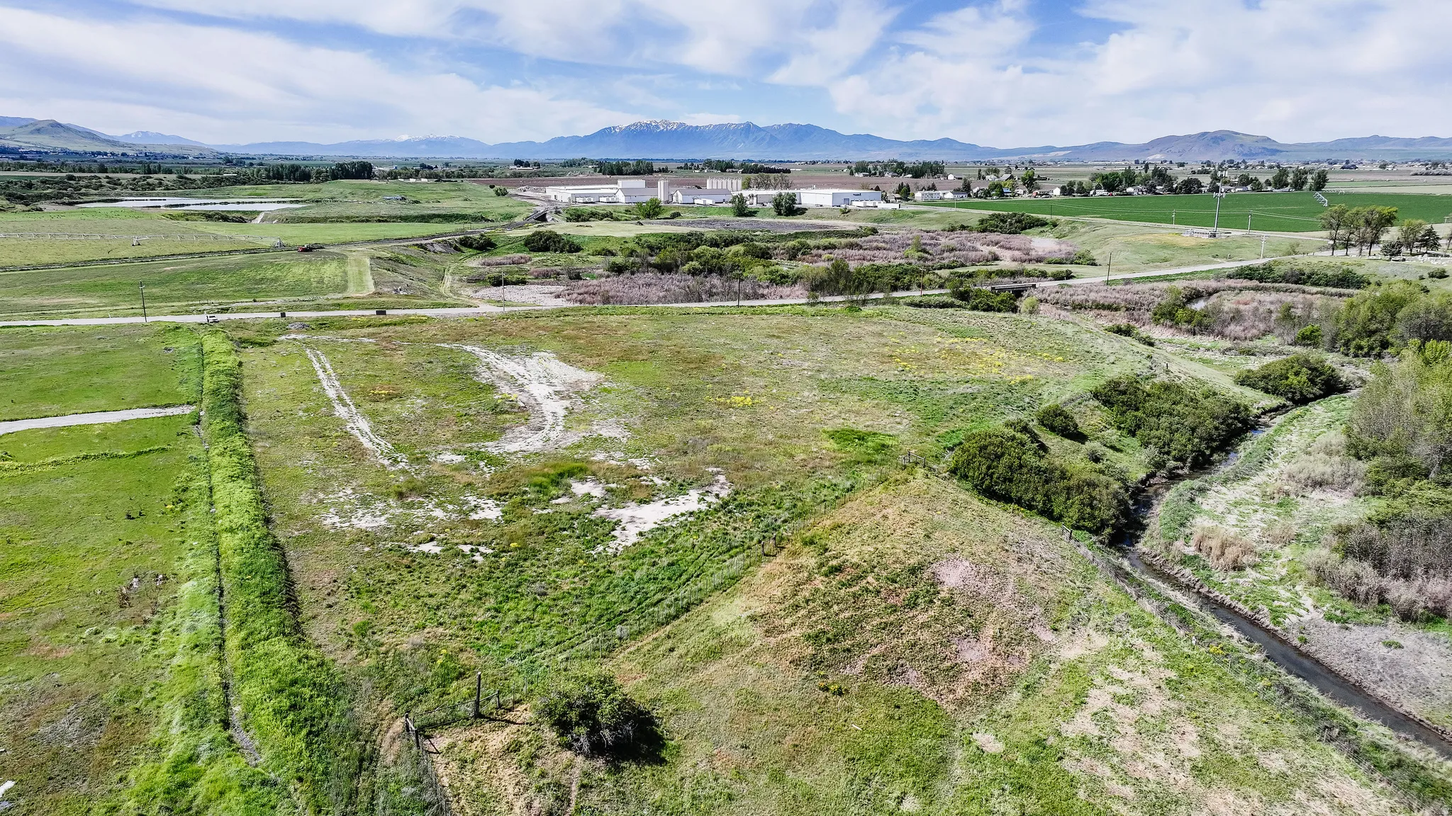 Expansive undeveloped lot featuring a natural water channel, mature vegetation, and distant mountain backdrops