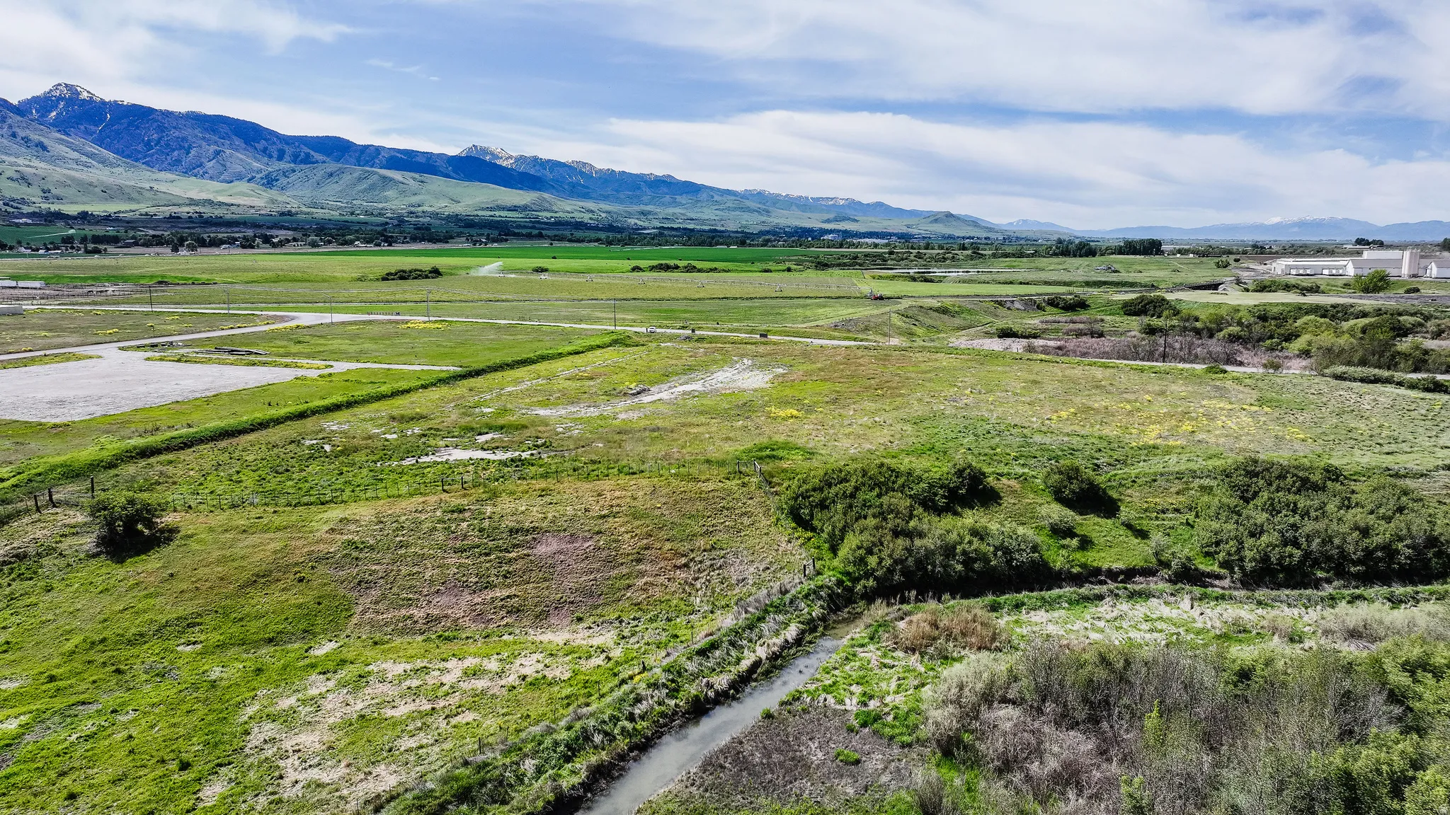 Expansive land parcel featuring open fields, a meandering stream, and lush green vegetation