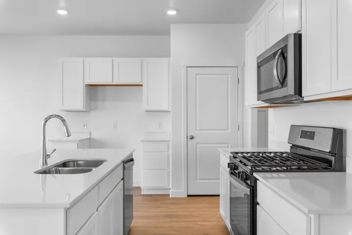 Kitchen with stainless steel appliances, white cabinets, light stone countertops, light wood-type flooring, and recessed lighting