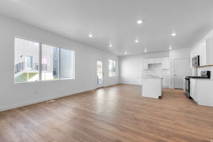 Kitchen with white cabinetry, open floor plan, stainless steel appliances, a center island with sink, and light wood finished floors