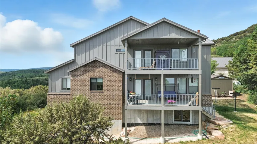 Back of property with board and batten siding, brick siding, french doors, a balcony, and a wooded view