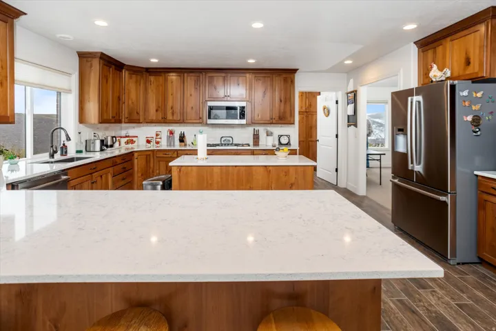 Kitchen with wood finish cabinetry, stainless steel appliances, wood finish floors, light stone counters, and recessed lighting