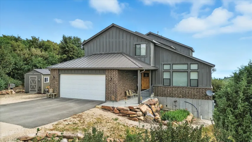 View of front of home with asphalt driveway, board and batten siding, brick siding, a garage, and a shed