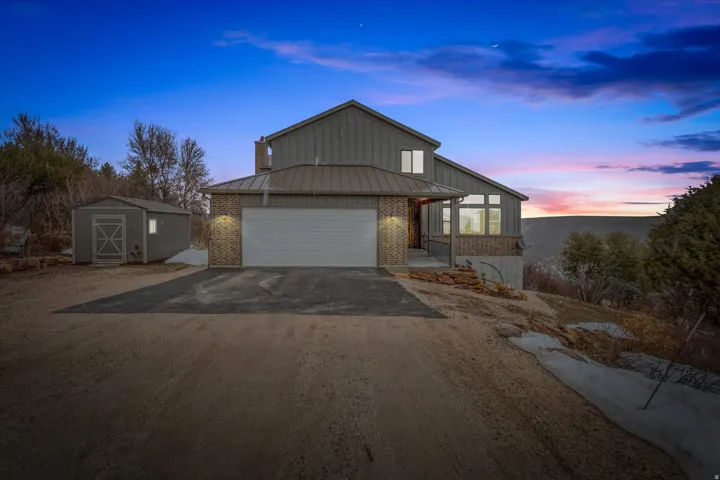 View of front of home with a standing seam roof, brick siding, driveway, and board and batten siding