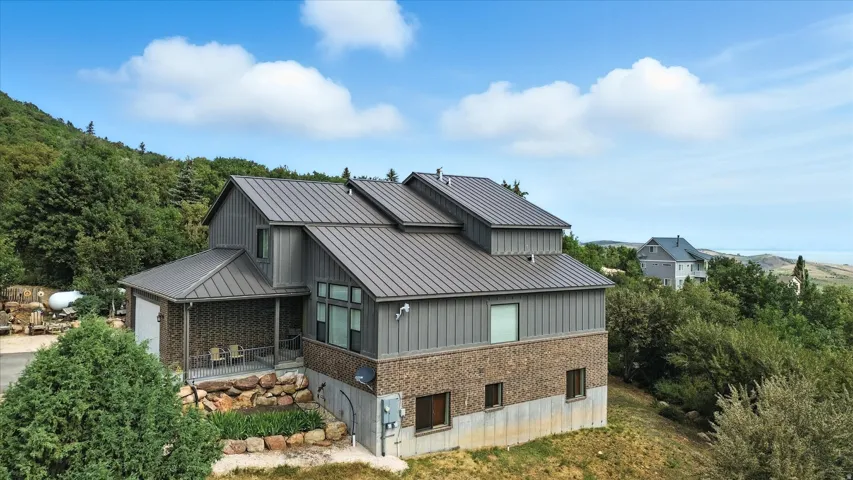 Rear view of property with brick siding, a patio area, a metal roof, and an attached garage