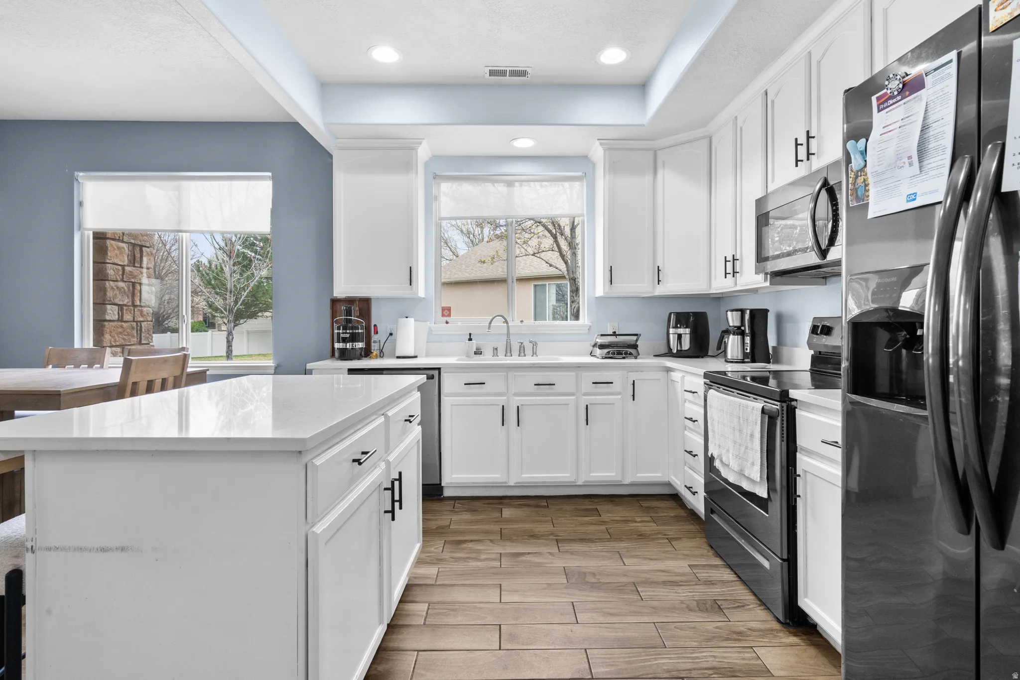 Kitchen featuring stainless steel appliances, white cabinets, wood finish floors, a center island, and light stone countertops