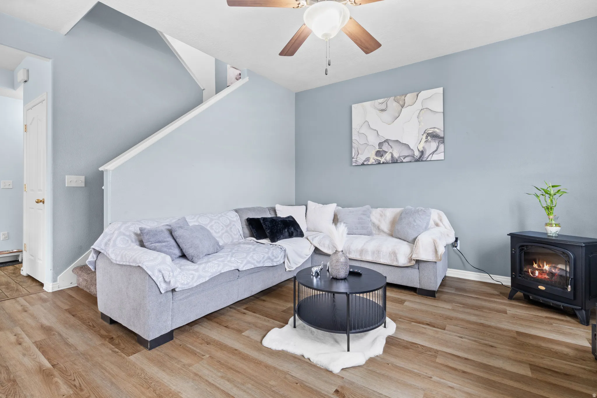 Living area with ceiling fan, light wood-style floors, and a wood stove