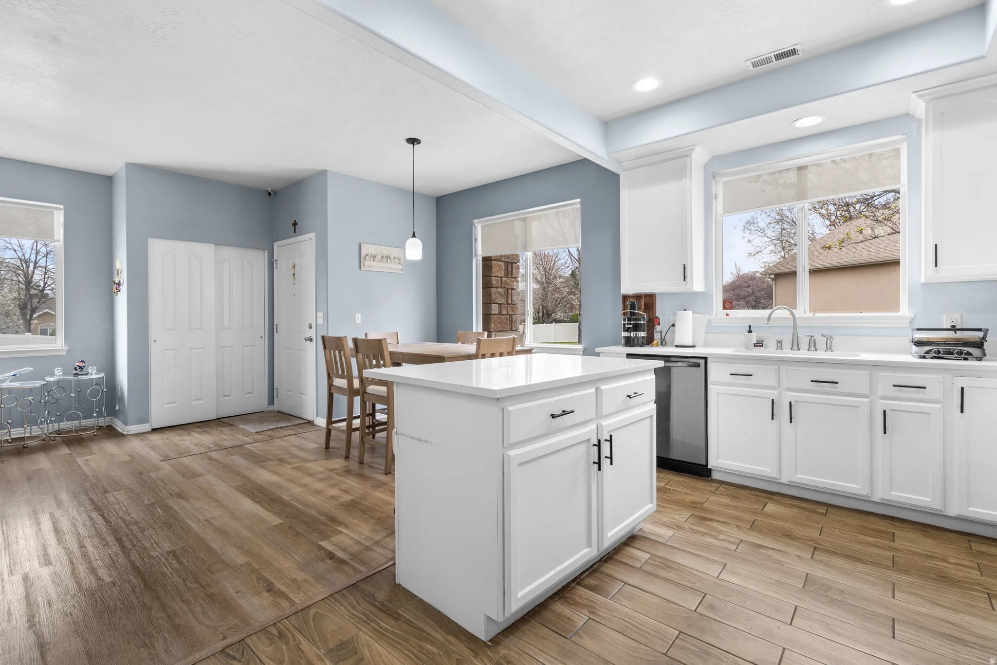 Kitchen featuring light wood finished floors, white cabinets, decorative light fixtures, and stainless steel dishwasher