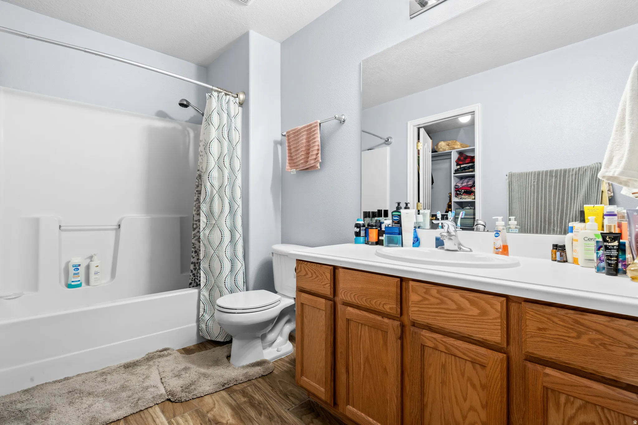 Full bathroom with vanity, dark wood-style floors, shower / bathtub combination with curtain, and a walk in closet