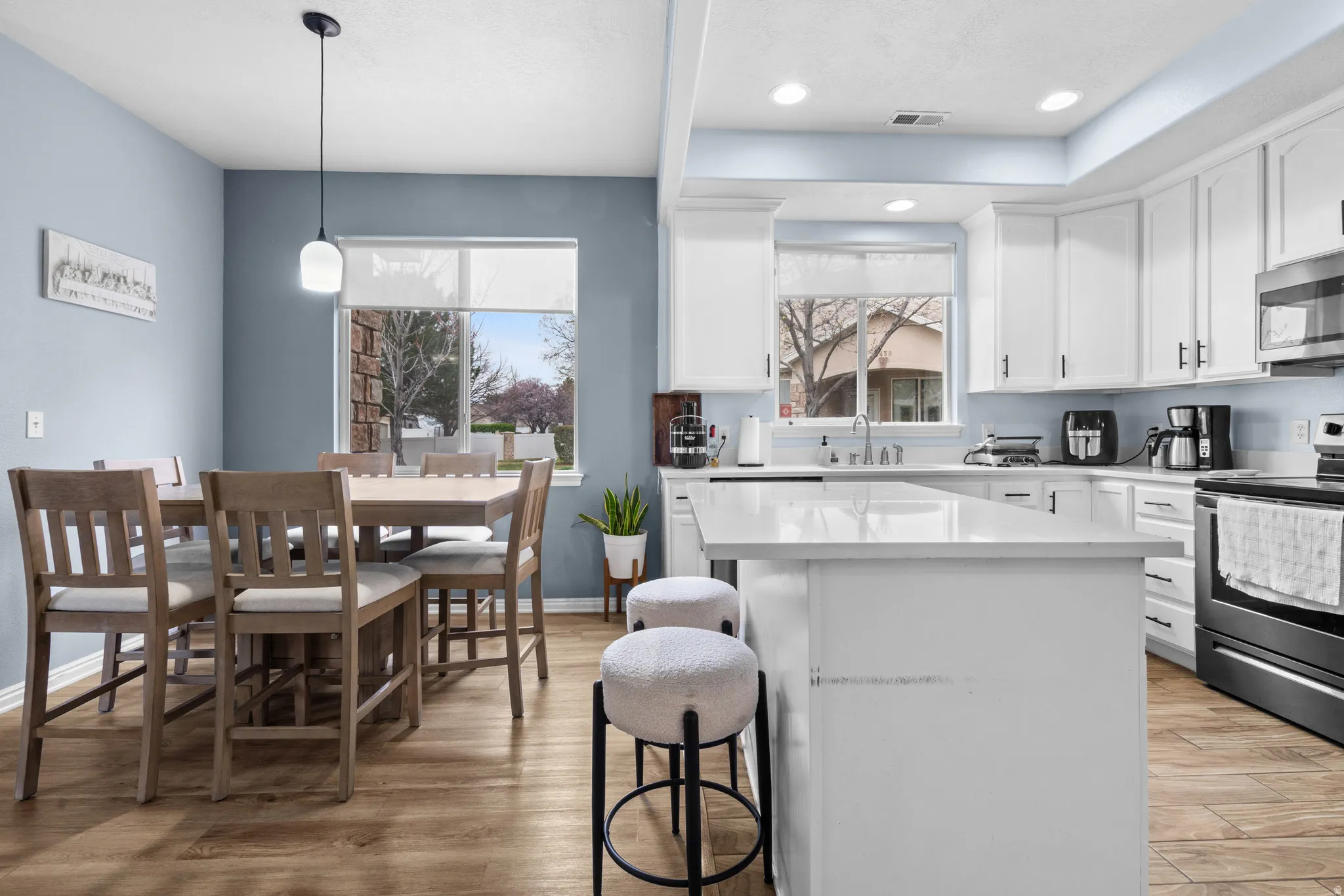 Kitchen with stainless steel appliances, white cabinets, light wood-style flooring, a kitchen island, and a breakfast bar