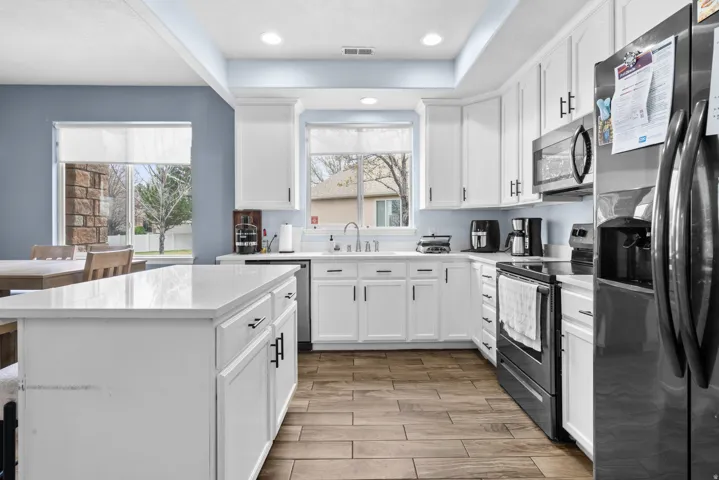 Kitchen featuring stainless steel appliances, white cabinets, wood finish floors, a center island, and light stone countertops
