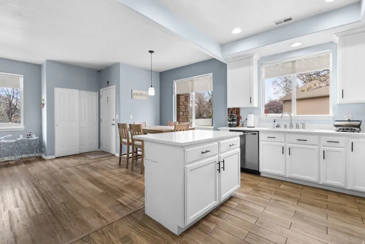 Kitchen featuring light wood finished floors, white cabinets, decorative light fixtures, and stainless steel dishwasher