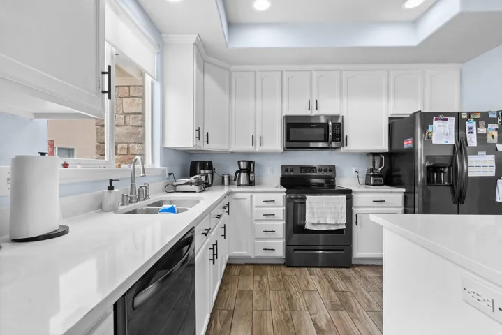 Kitchen featuring white cabinetry, stainless steel appliances, a tray ceiling, light wood-style floors, and light stone countertops