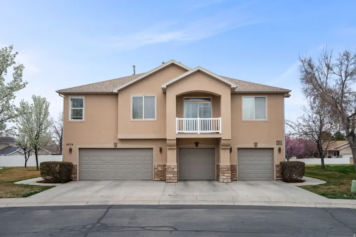 View of front of property featuring a balcony, an attached garage, stucco siding, and driveway