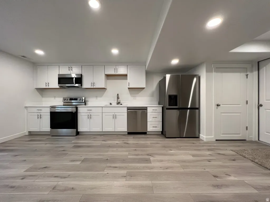 Kitchen featuring light countertops, stainless steel appliances, light wood-style floors, white cabinetry, and recessed lighting