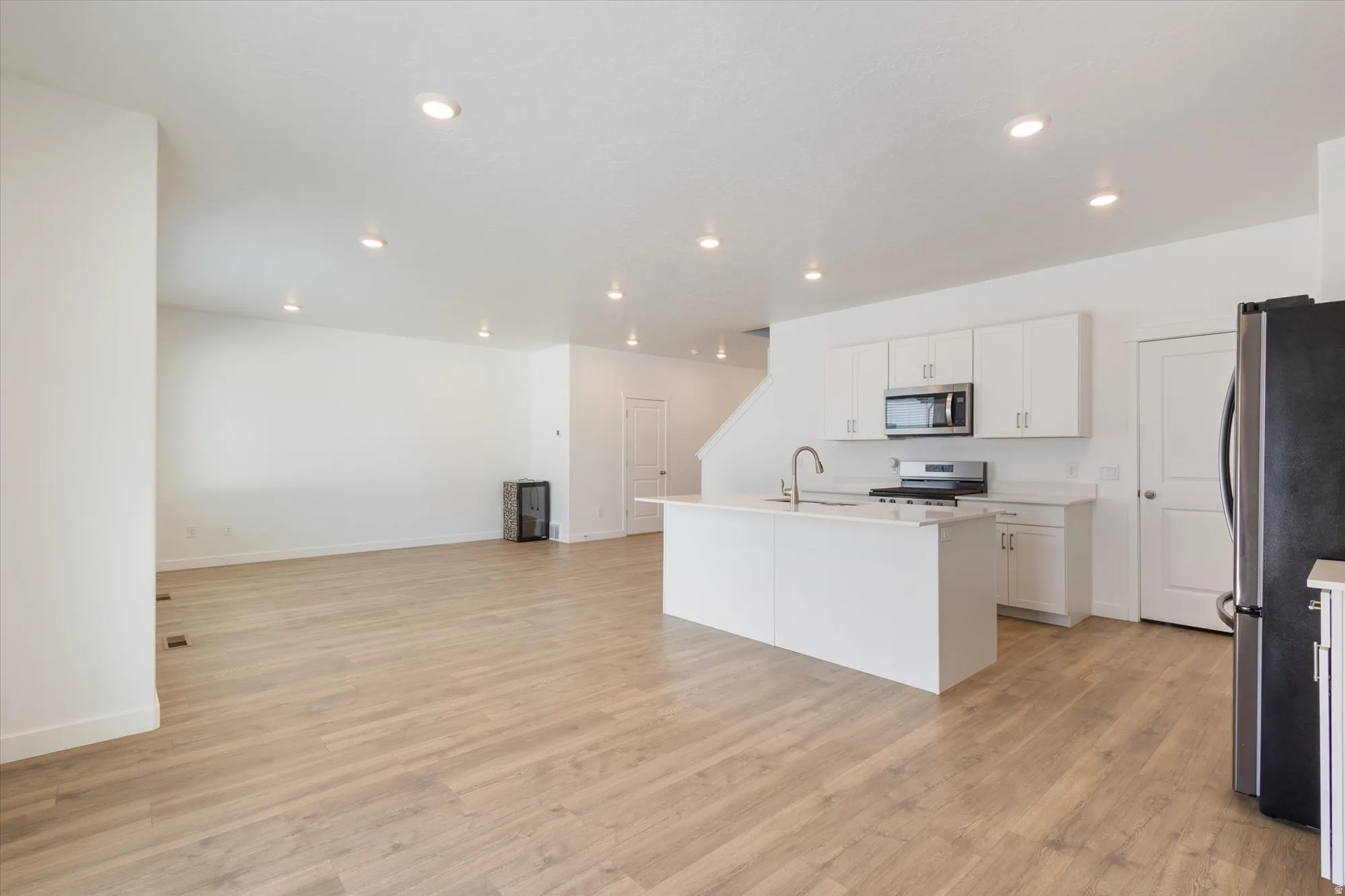 Kitchen with stainless steel appliances, an island with sink, light wood-style floors, white cabinets, and recessed lighting
