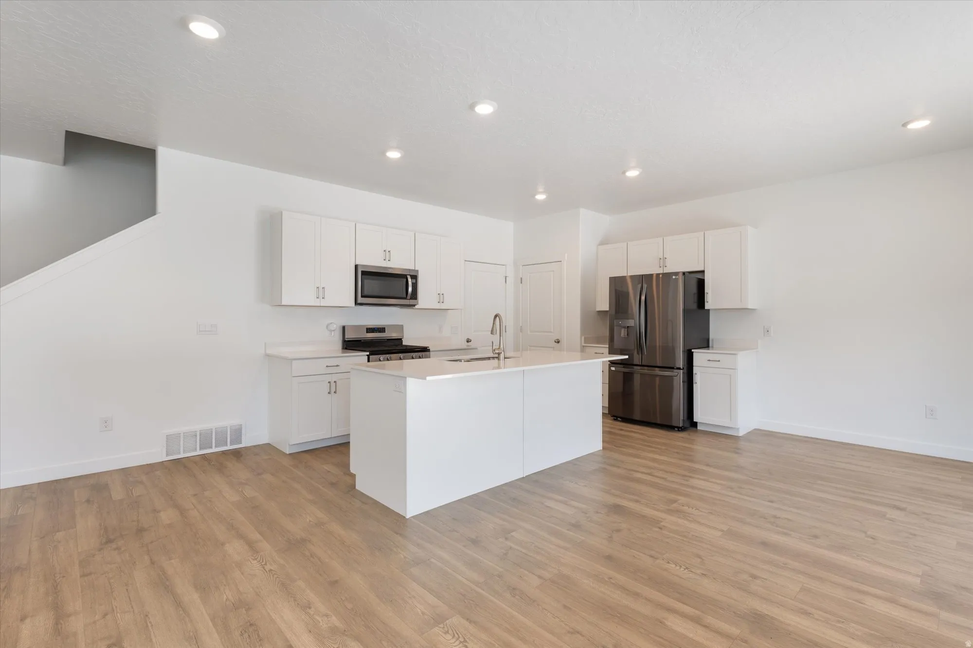 Kitchen with stainless steel appliances, light countertops, white cabinetry, an island with sink, and light wood-type flooring