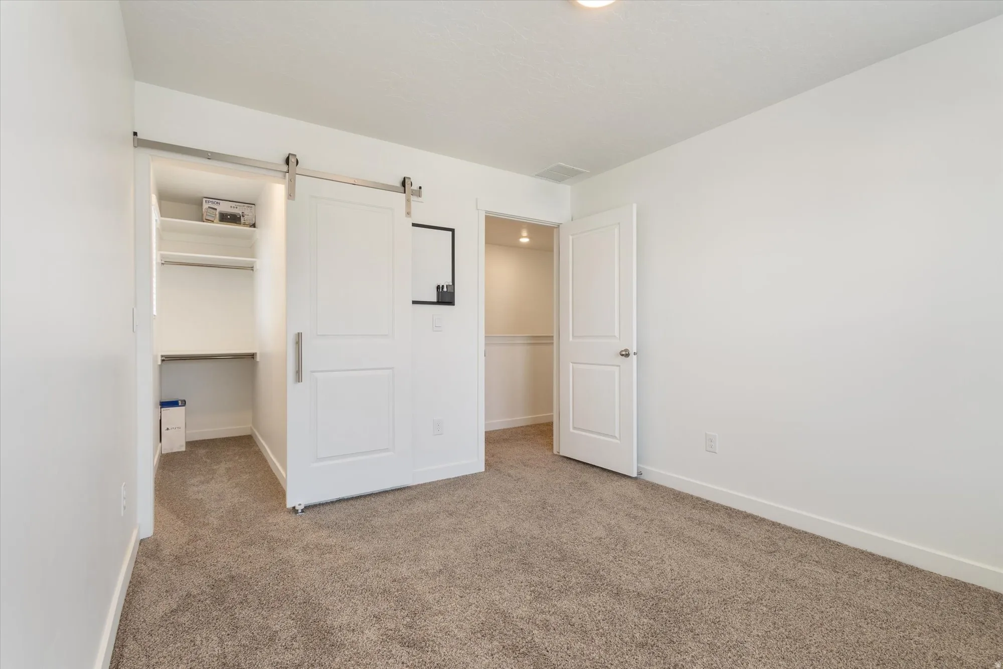 Unfurnished bedroom featuring a barn door, carpet floors, and a walk in closet