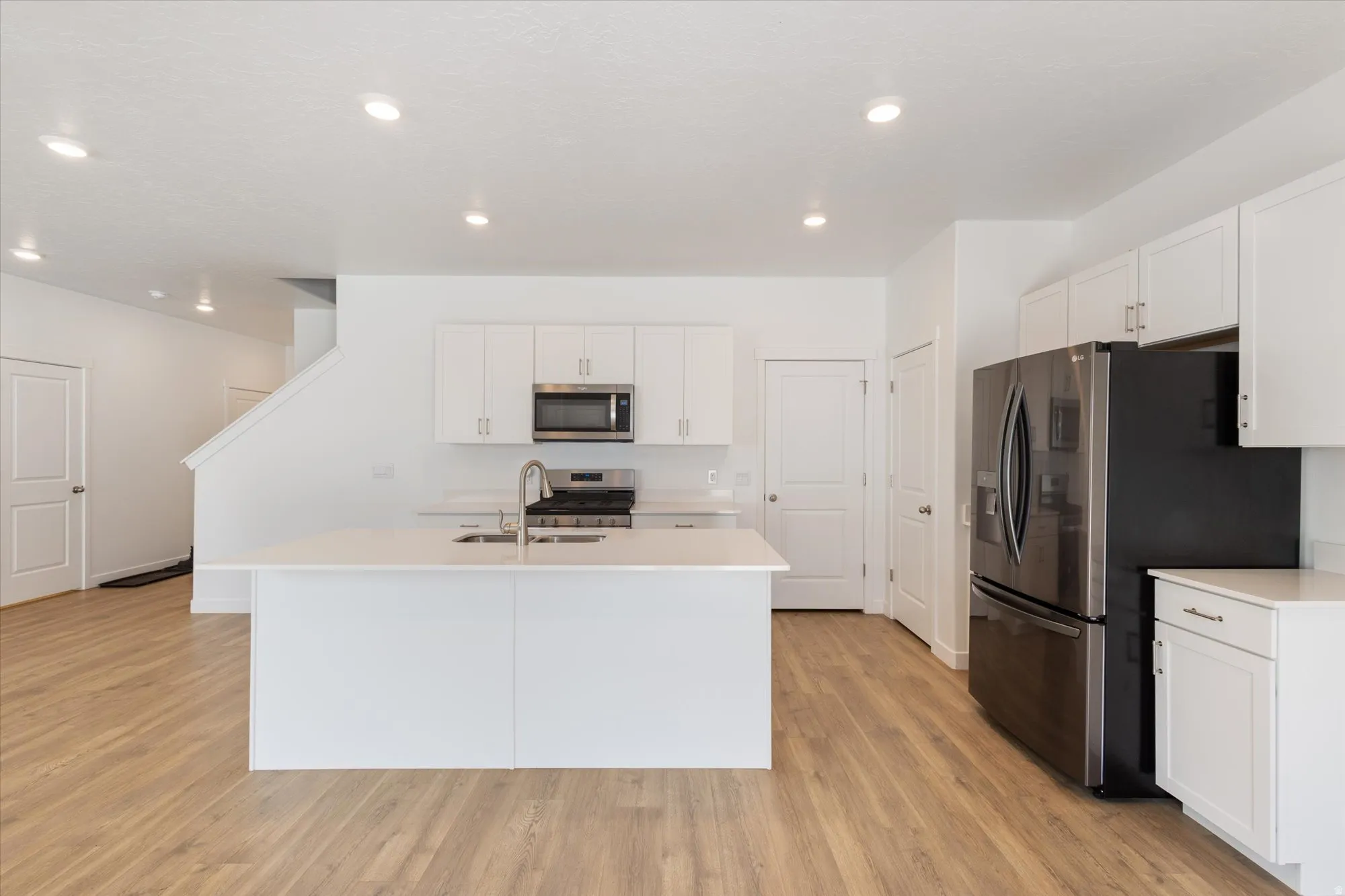 Kitchen featuring stainless steel appliances, light wood finished floors, white cabinetry, a kitchen island with sink, and recessed lighting