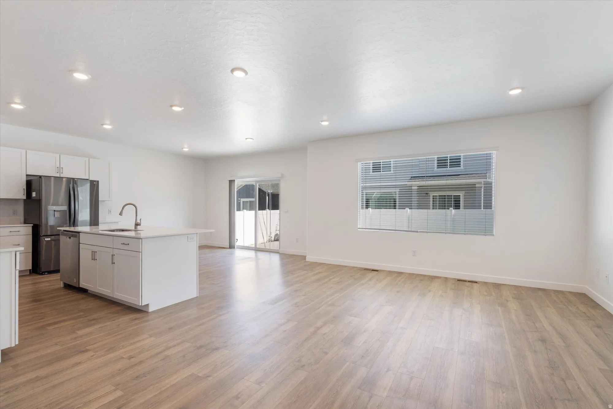 Kitchen featuring open floor plan, an island with sink, light wood-style floors, stainless steel appliances, and white cabinets