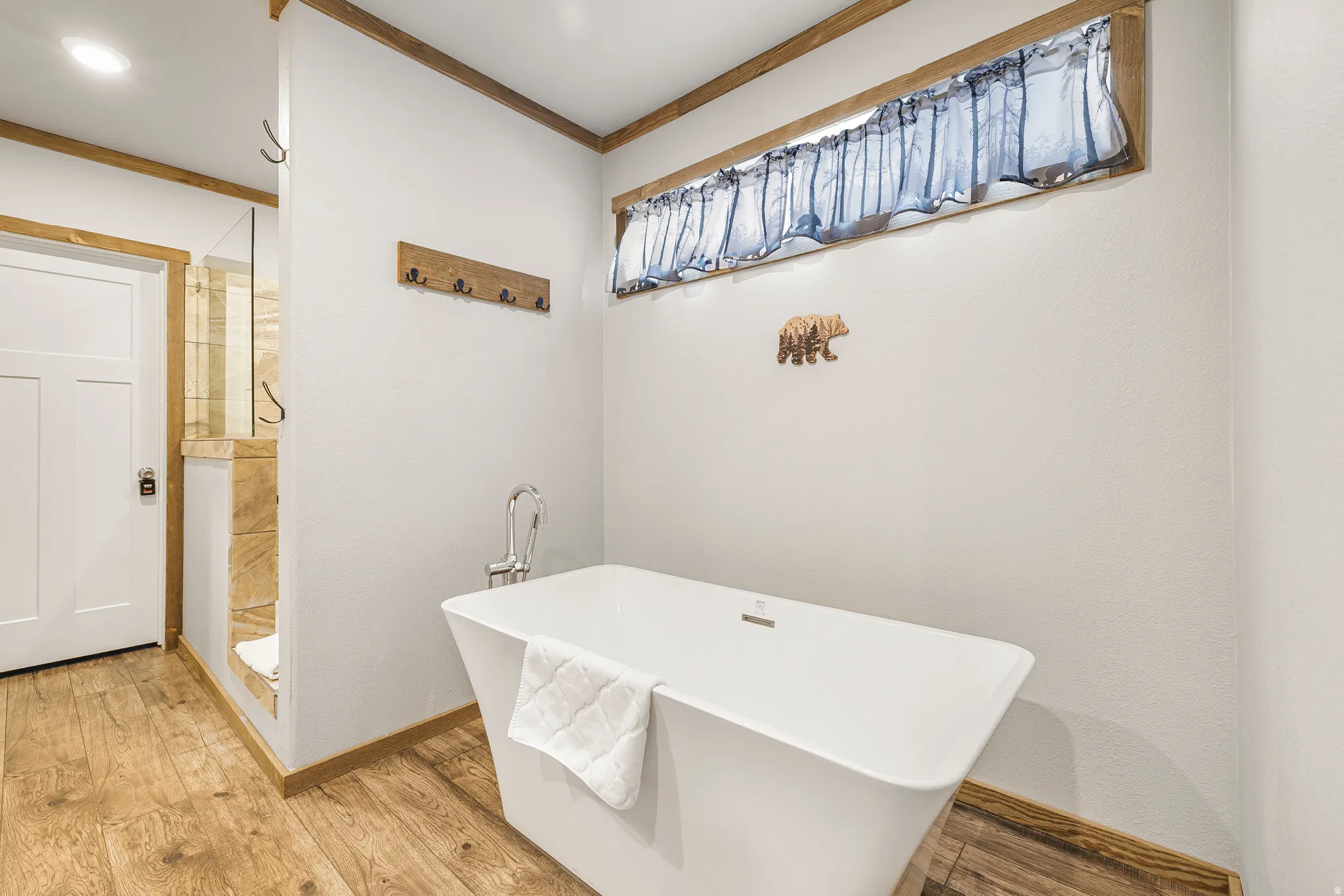 Full bathroom with ornamental molding, a freestanding tub, light wood-style floors, and a tile shower