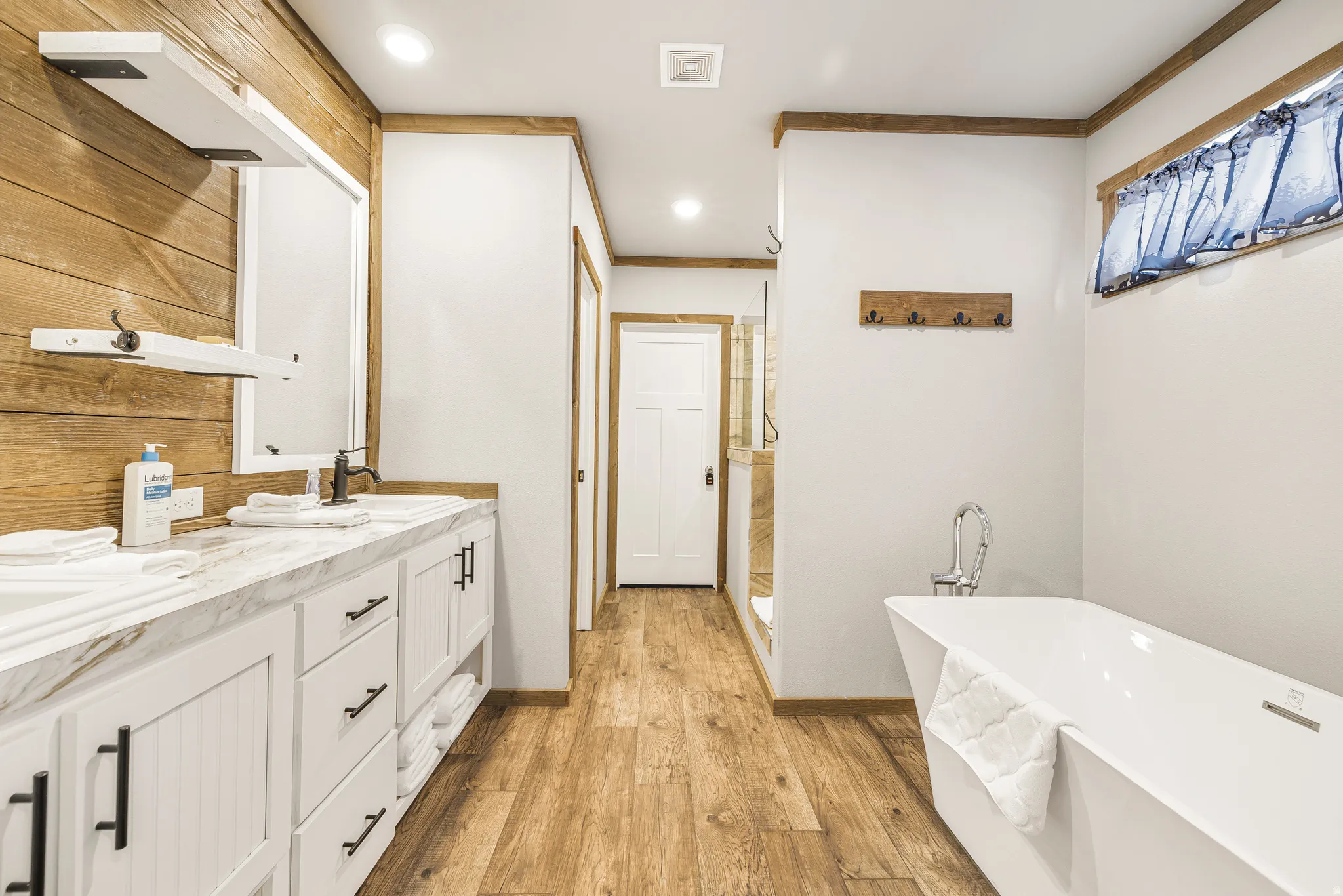 Full bathroom with a freestanding tub, double vanity, a stall shower, ornamental molding, and light wood-type flooring