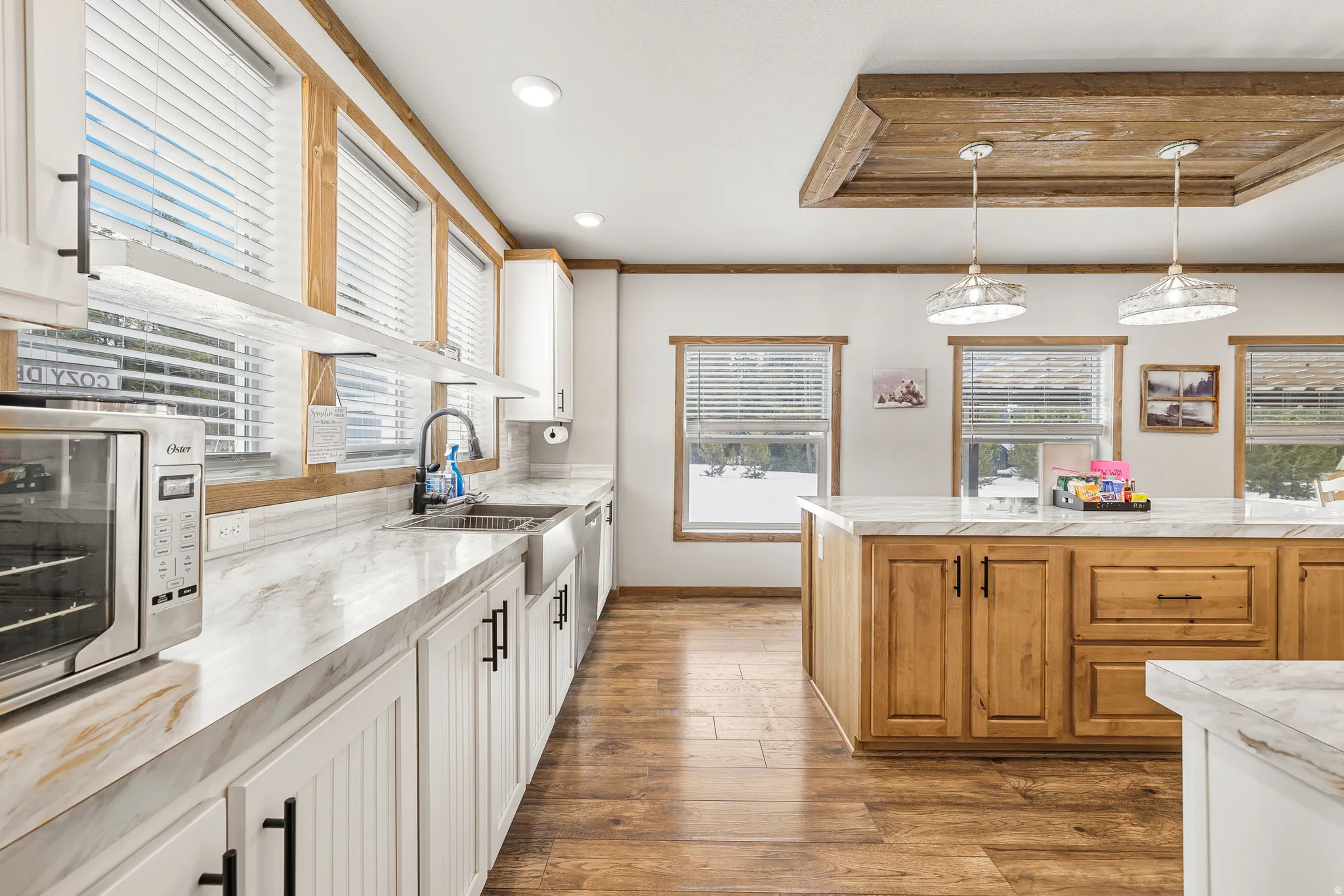 Kitchen with two tone cabinetry, a raised ceiling, dark wood-style flooring, and pendant lighting