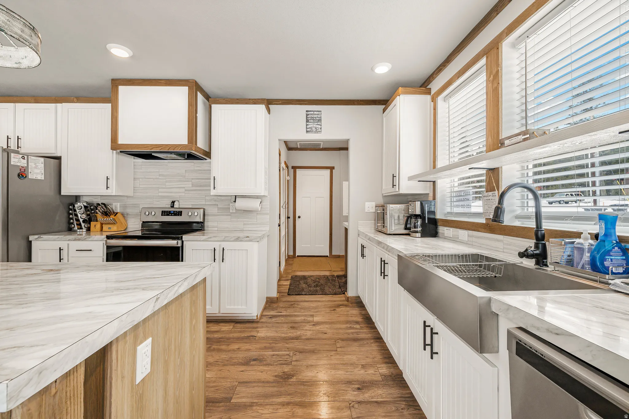 Kitchen featuring dual tone cabinets, stainless steel appliances, dark wood finished floors, decorative backsplash, and light stone countertops