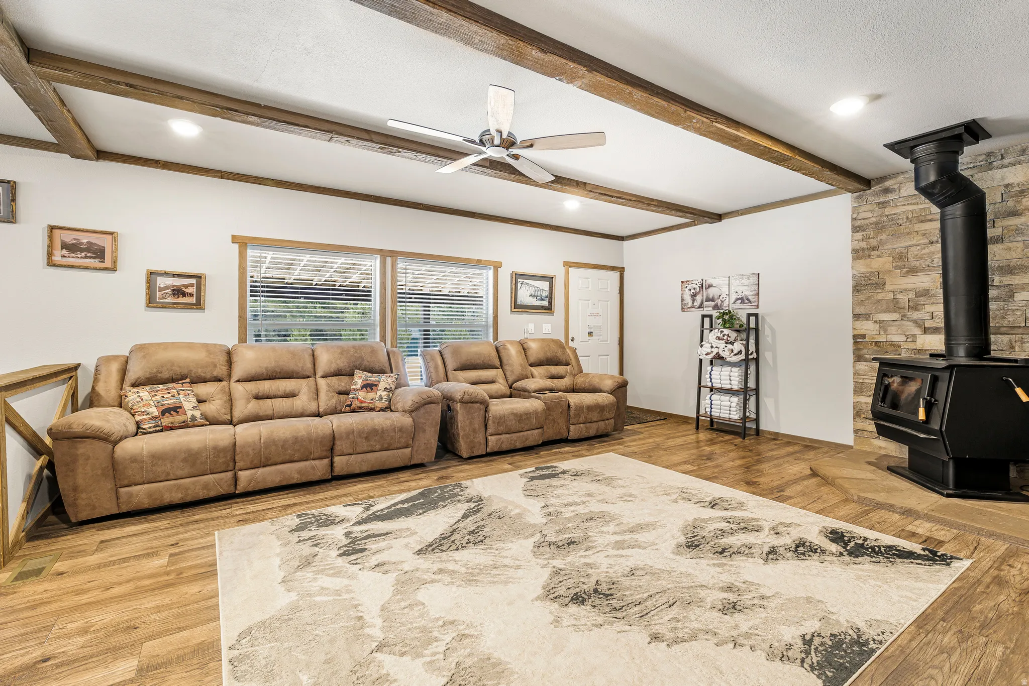 Living room with ceiling fan, a wood stove, beamed ceiling, light wood-type flooring, and recessed lighting