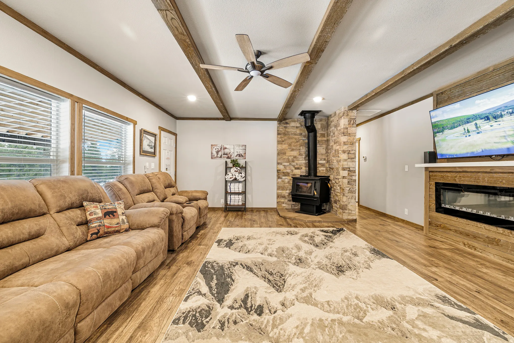 Living room with a ceiling fan, a wood stove, light wood-style flooring, crown molding, and beam ceiling