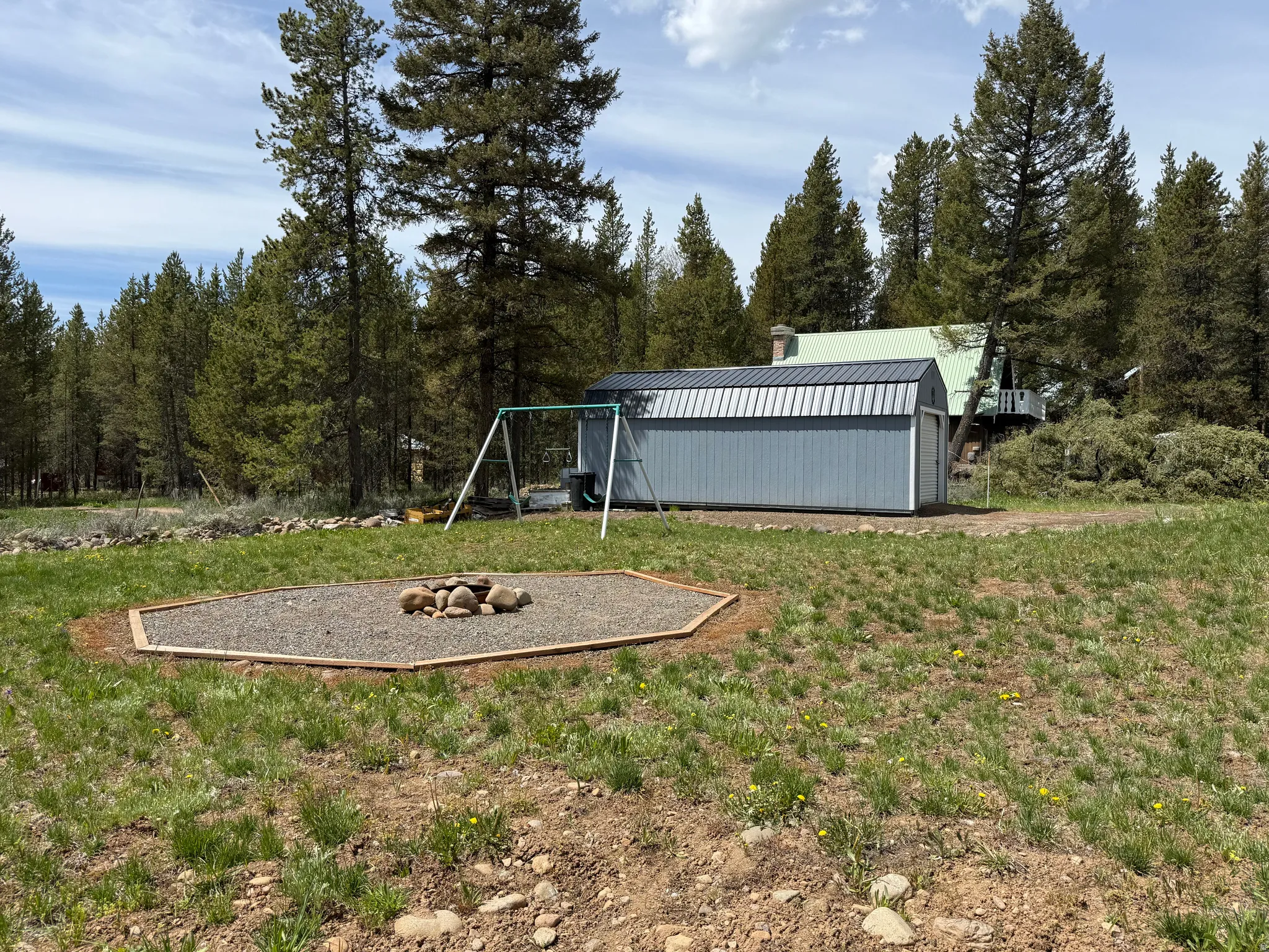 Gravel fire pit area with timber border, surrounded by a grassy expanse and mature evergreen trees