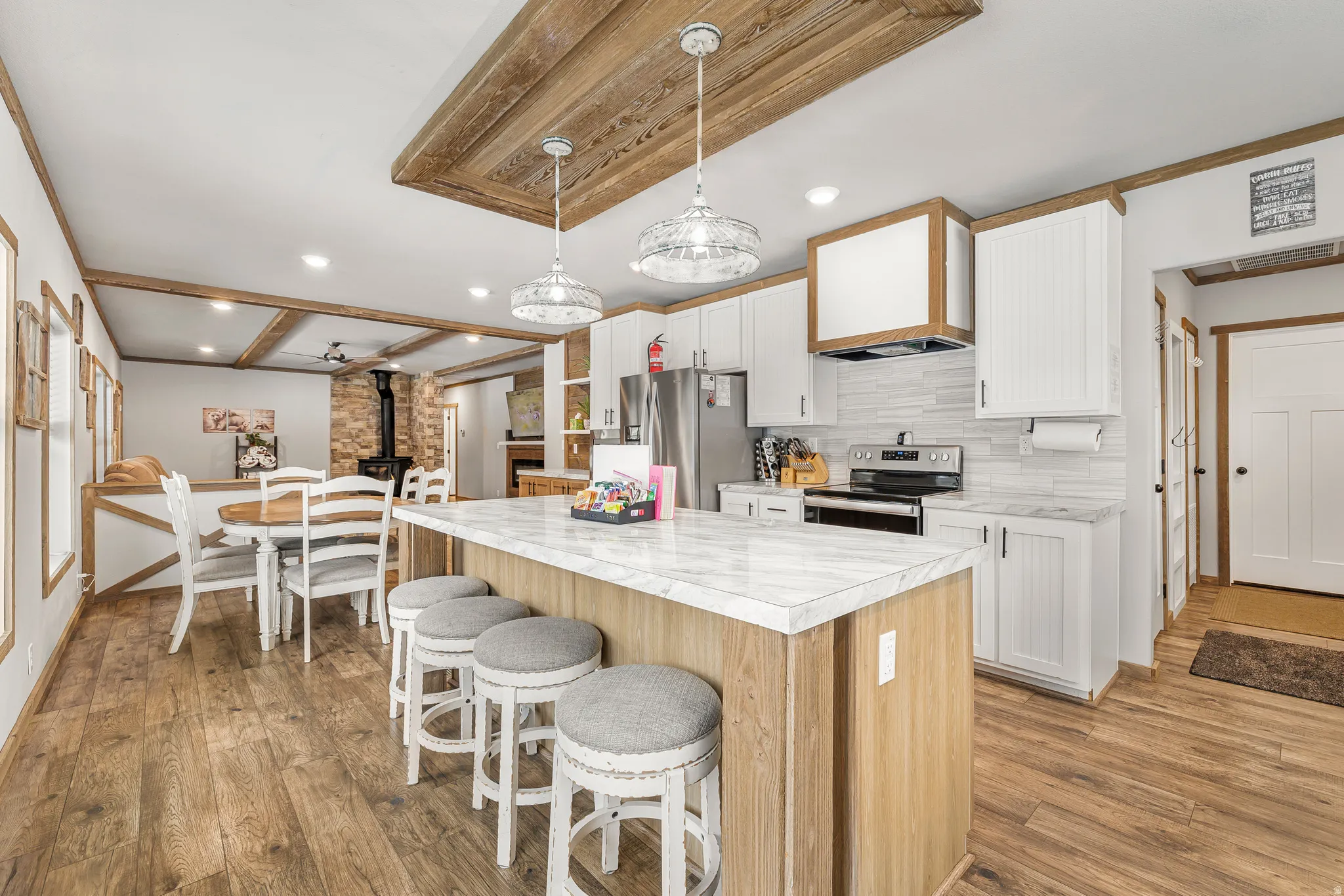 Two tone kitchen featuring a wood stove, a center island, dual tone cabinetry, light countertops, and a kitchen breakfast bar