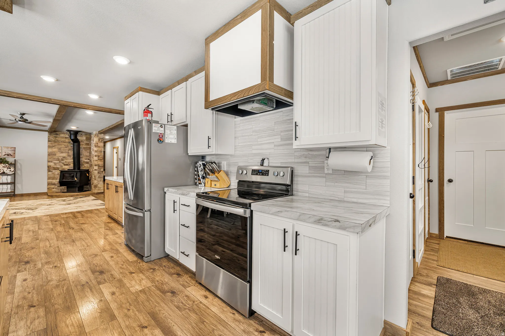 Kitchen featuring a wood stove, stainless steel appliances, light countertops, white cabinets, and recessed lighting
