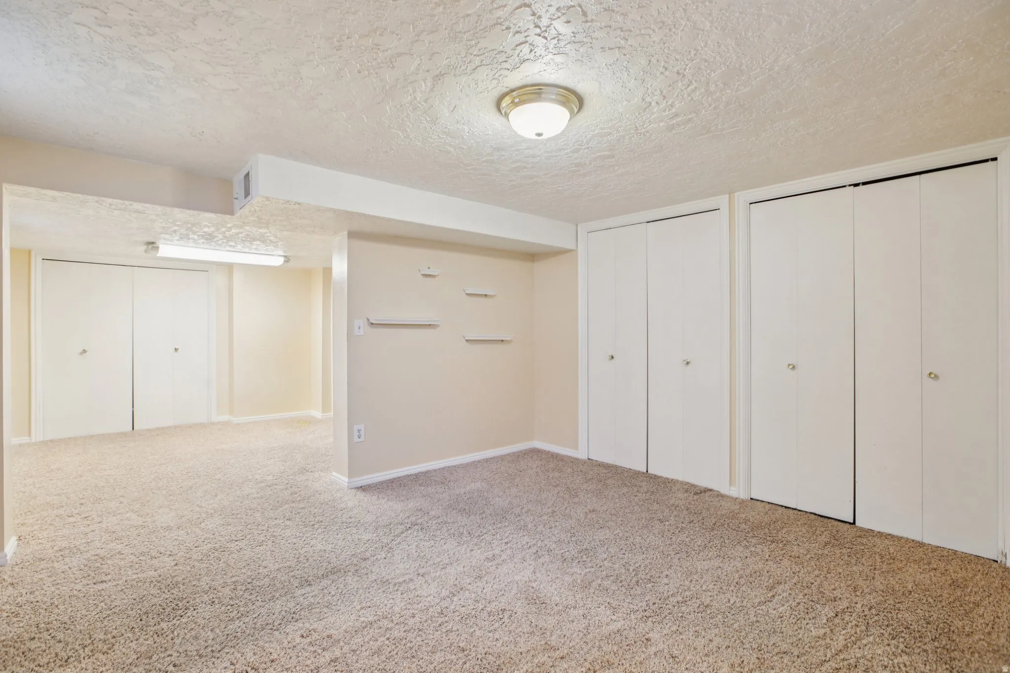 Unfurnished bedroom with a textured ceiling, two closets, and light carpet