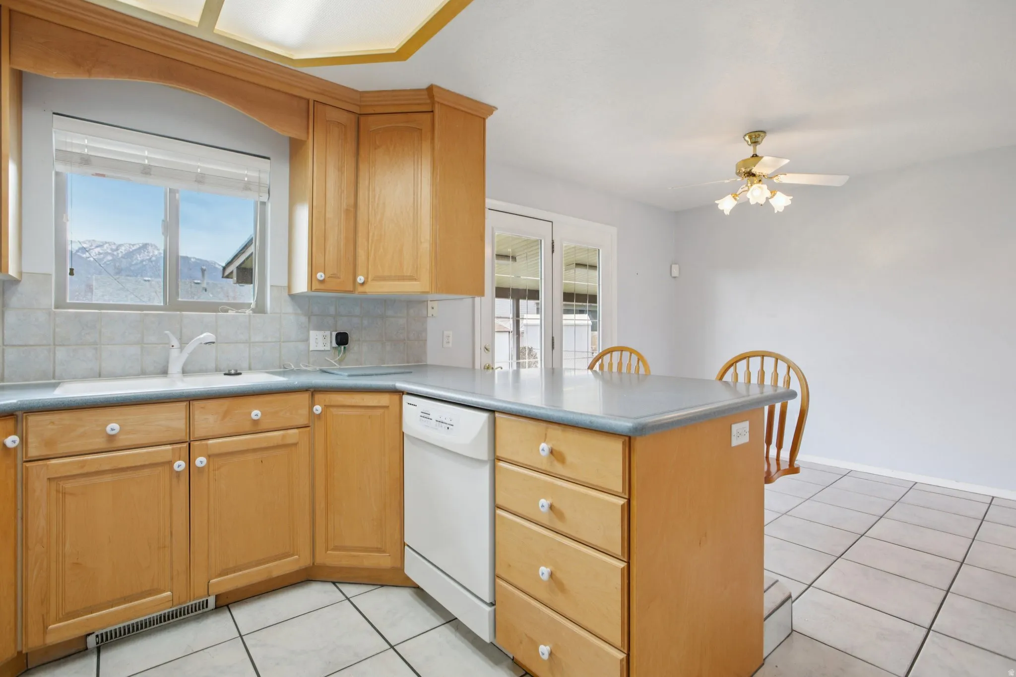 Kitchen featuring a peninsula, backsplash, light tile patterned flooring, and white dishwasher