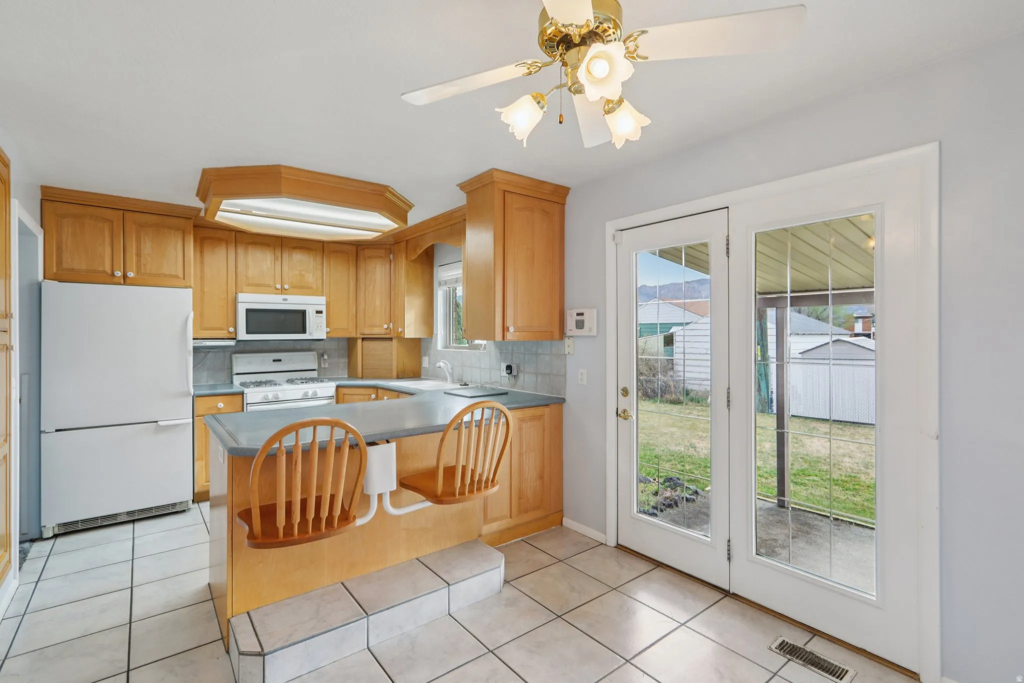 Kitchen with white appliances, light tile patterned flooring, tasteful backsplash, and ceiling fan