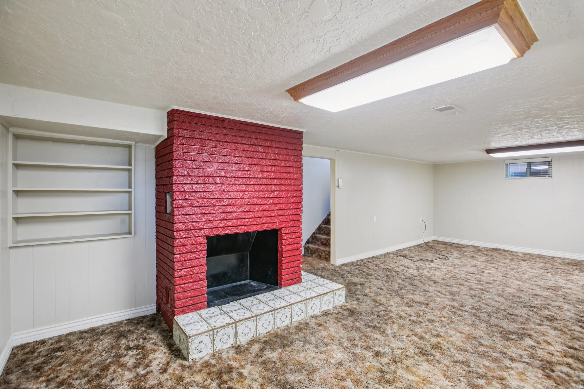 Unfurnished living room featuring a textured ceiling, carpet flooring, and a brick fireplace