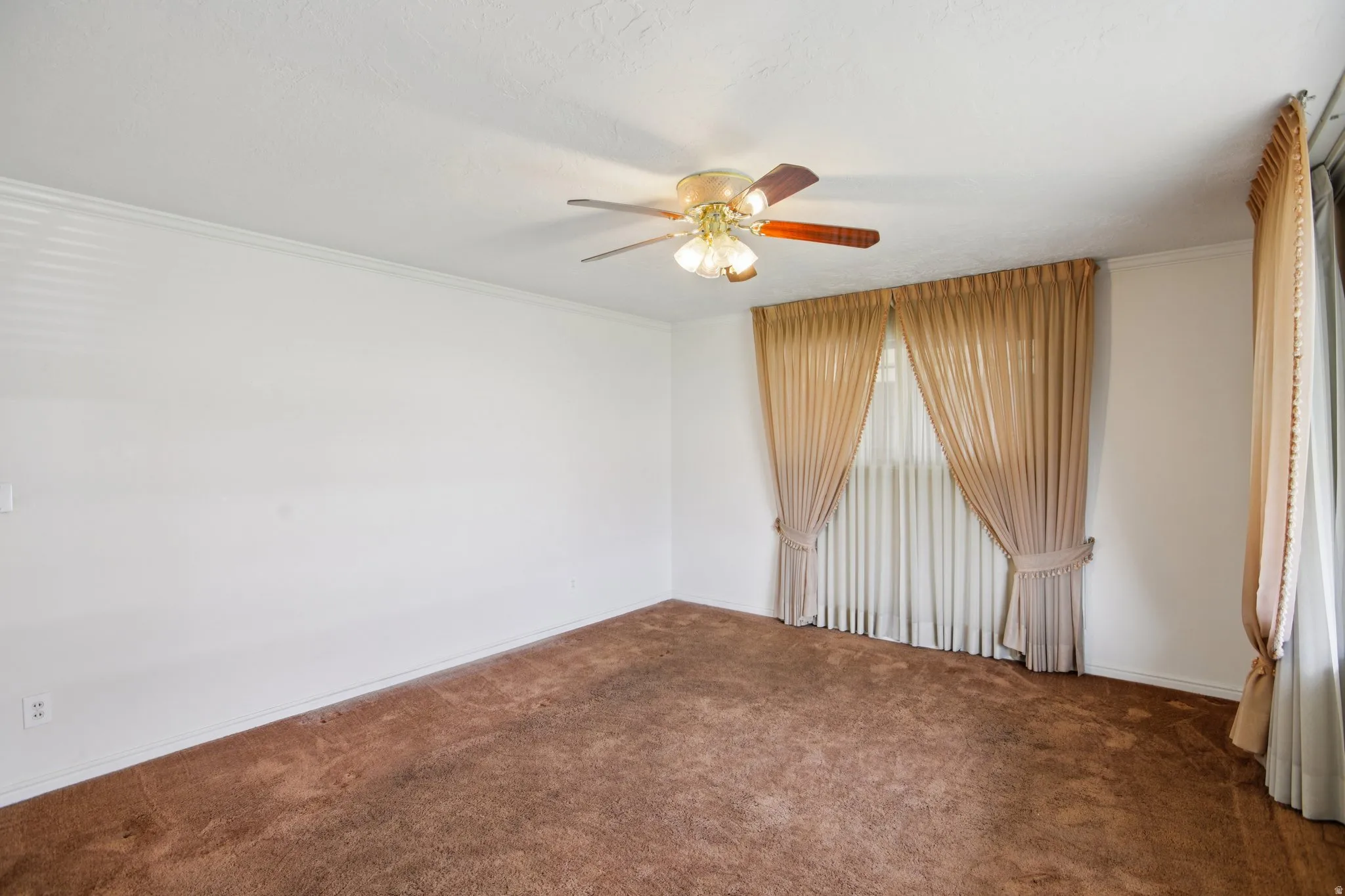Empty room featuring dark carpet, a ceiling fan, and ornamental molding