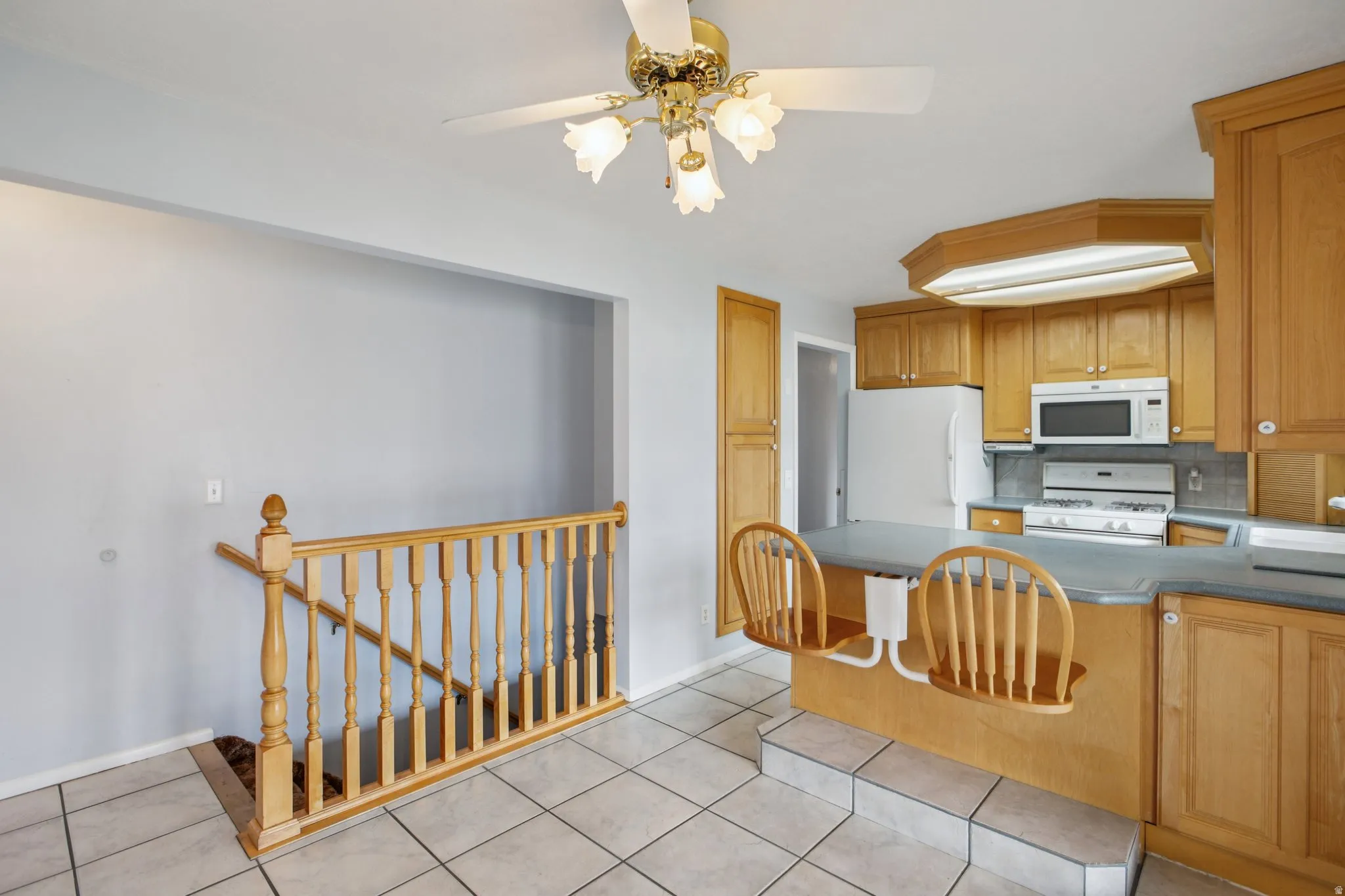 Kitchen with dark countertops, white appliances, a peninsula, light tile patterned flooring, and backsplash