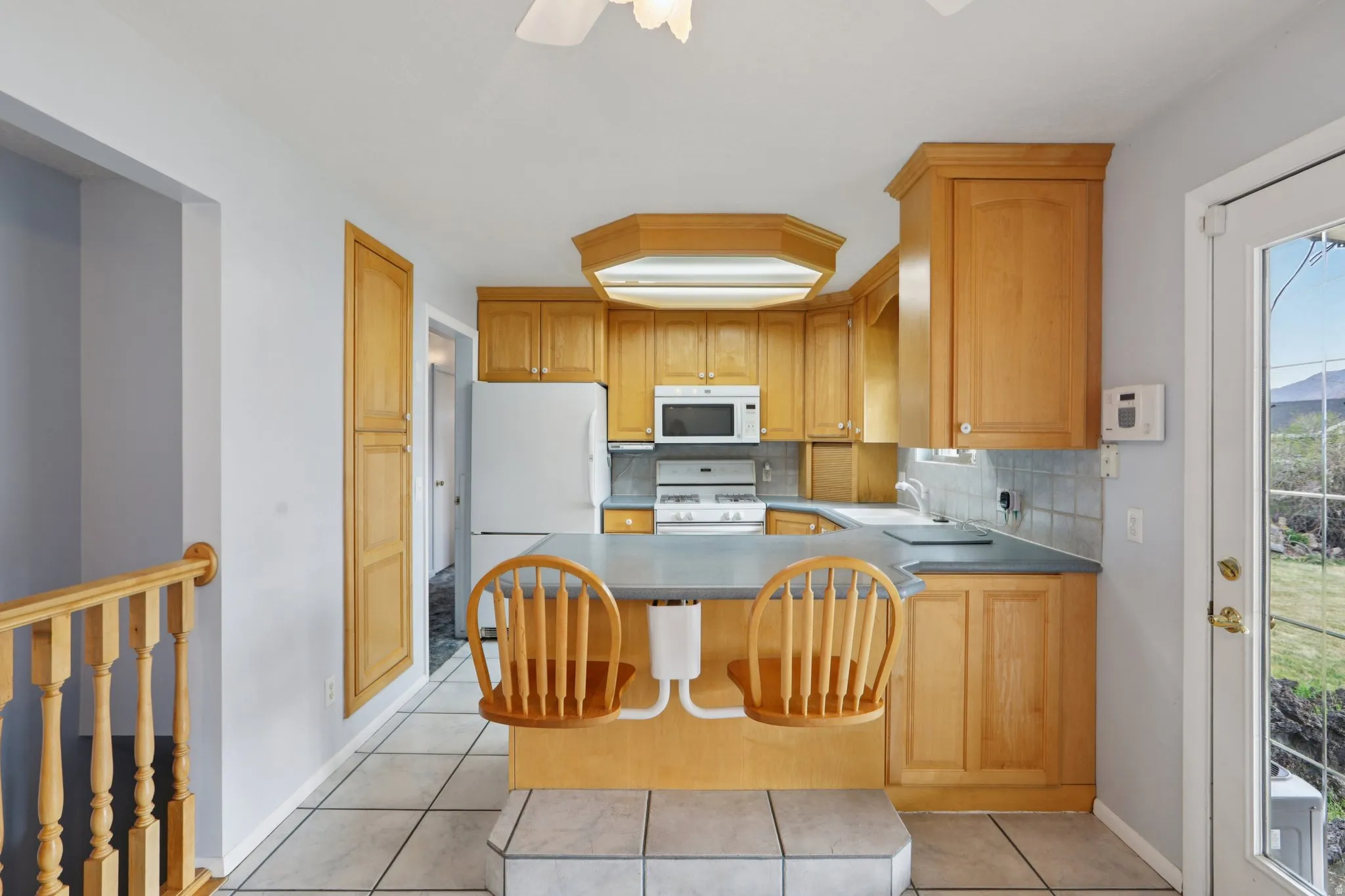 Kitchen with decorative backsplash, white appliances, a peninsula, ceiling fan, and light tile patterned flooring