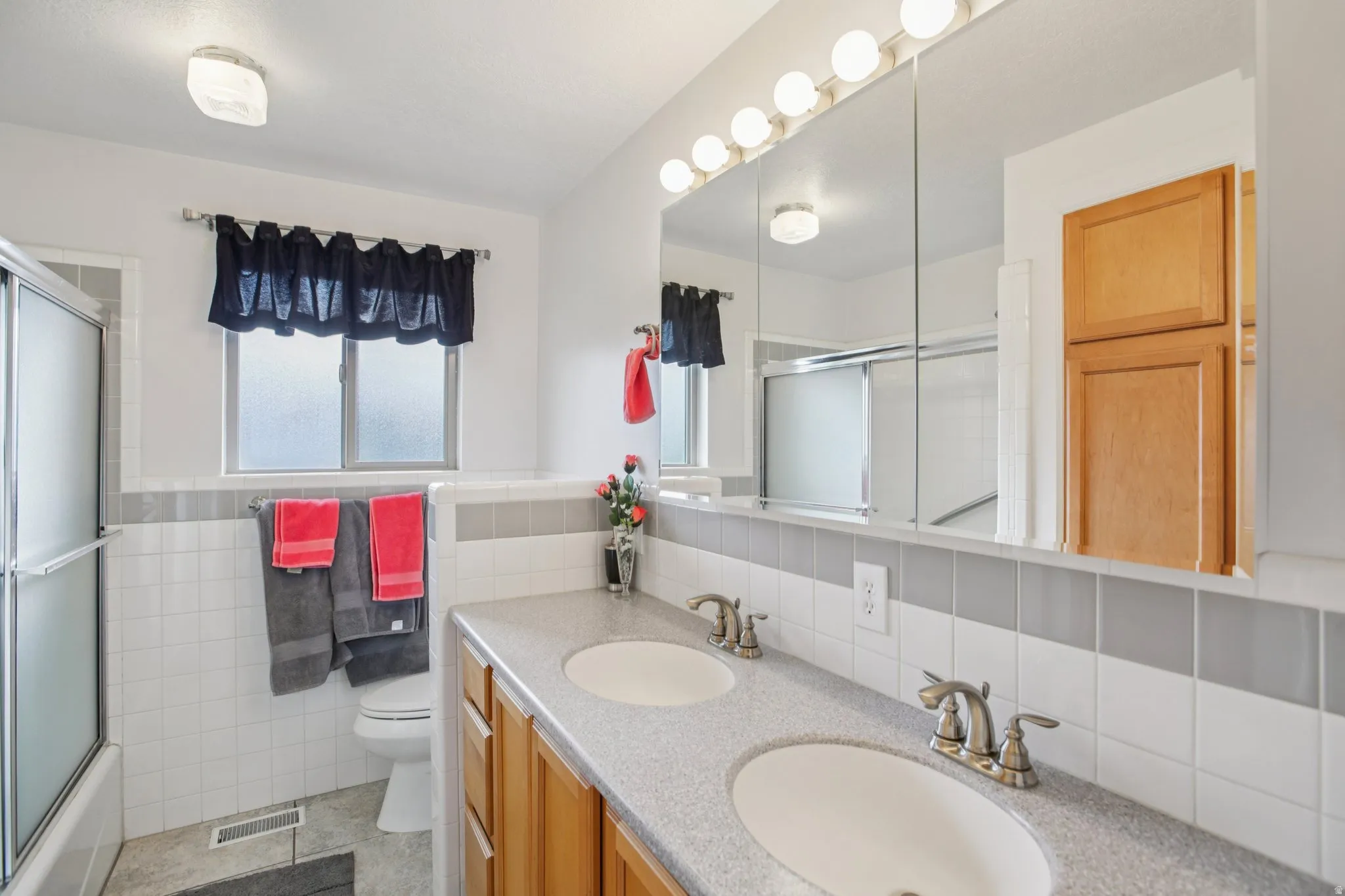 Full bathroom with double vanity, combined bath / shower with glass door, a wainscoted wall, and tile walls