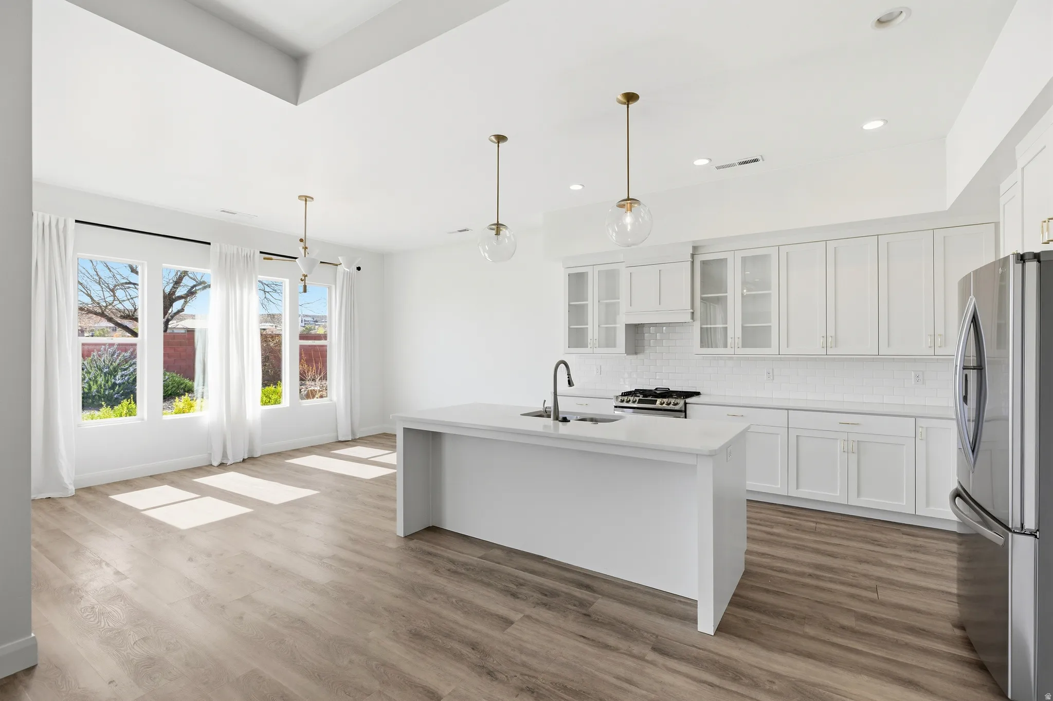 Kitchen with stainless steel appliances, white cabinetry, glass fronted cabinets, a center island with sink, and decorative light fixtures