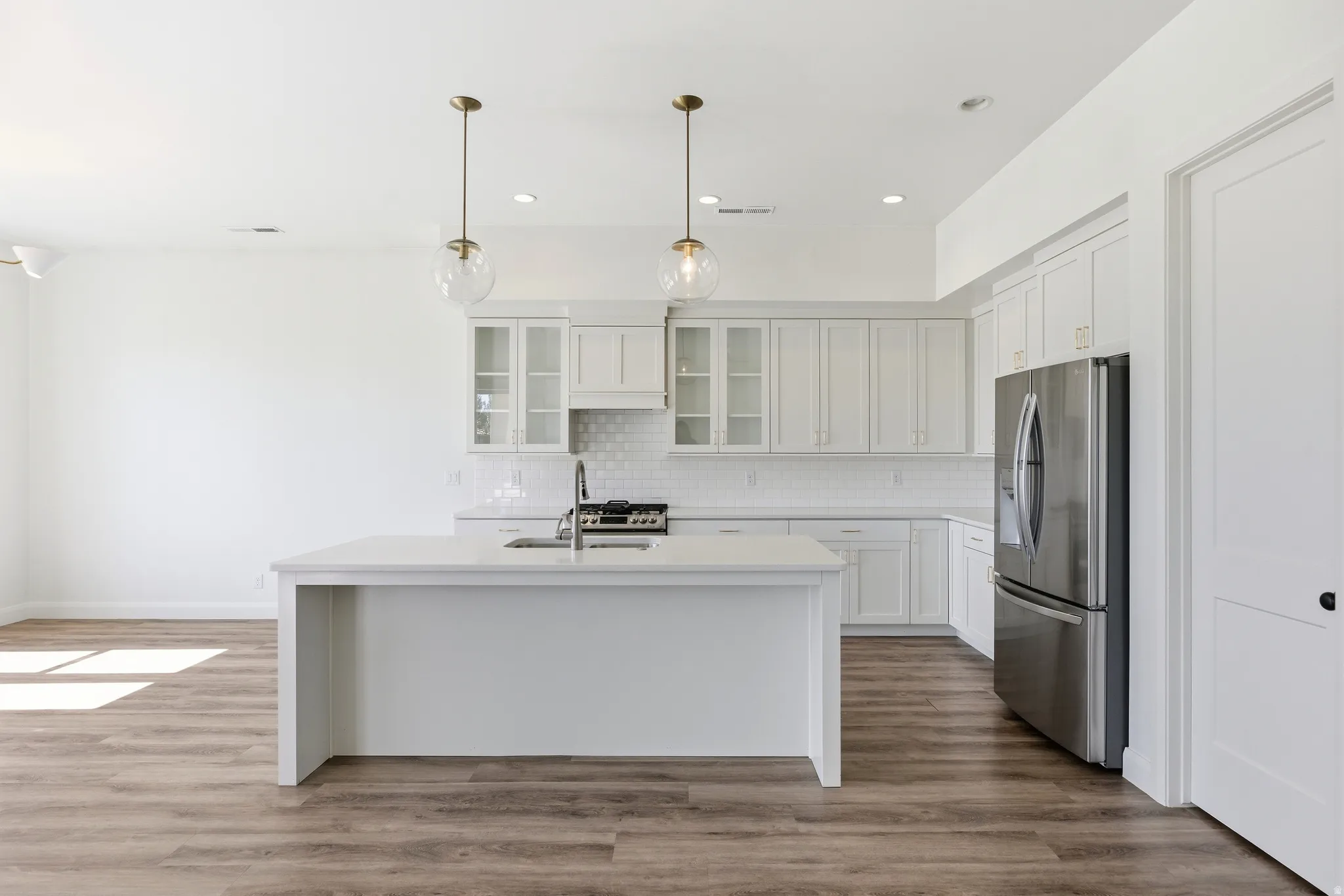 Kitchen featuring stainless steel appliances, glass insert cabinets, a kitchen island with sink, white cabinetry, and light wood-style flooring